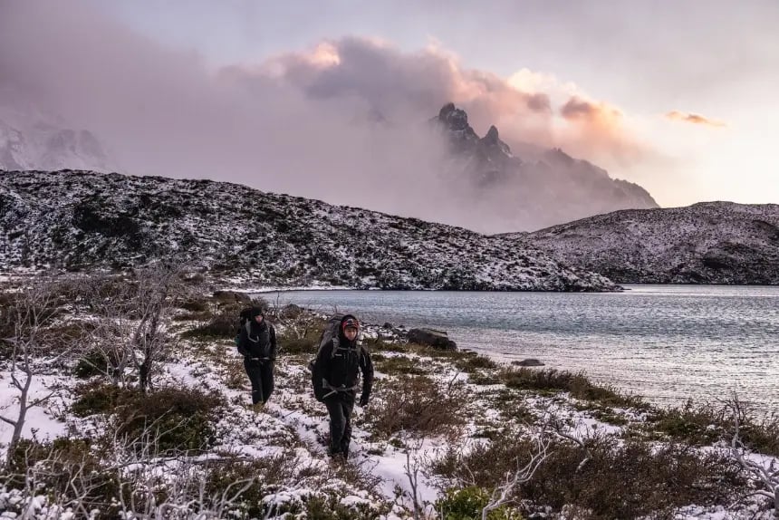 Alt text: dos excursionistas caminando cerca de un lago en el Parque Nacional Torres del Paine en invierno